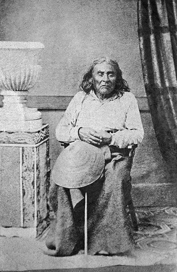 An old photograph of a man sitting in front of a vase.