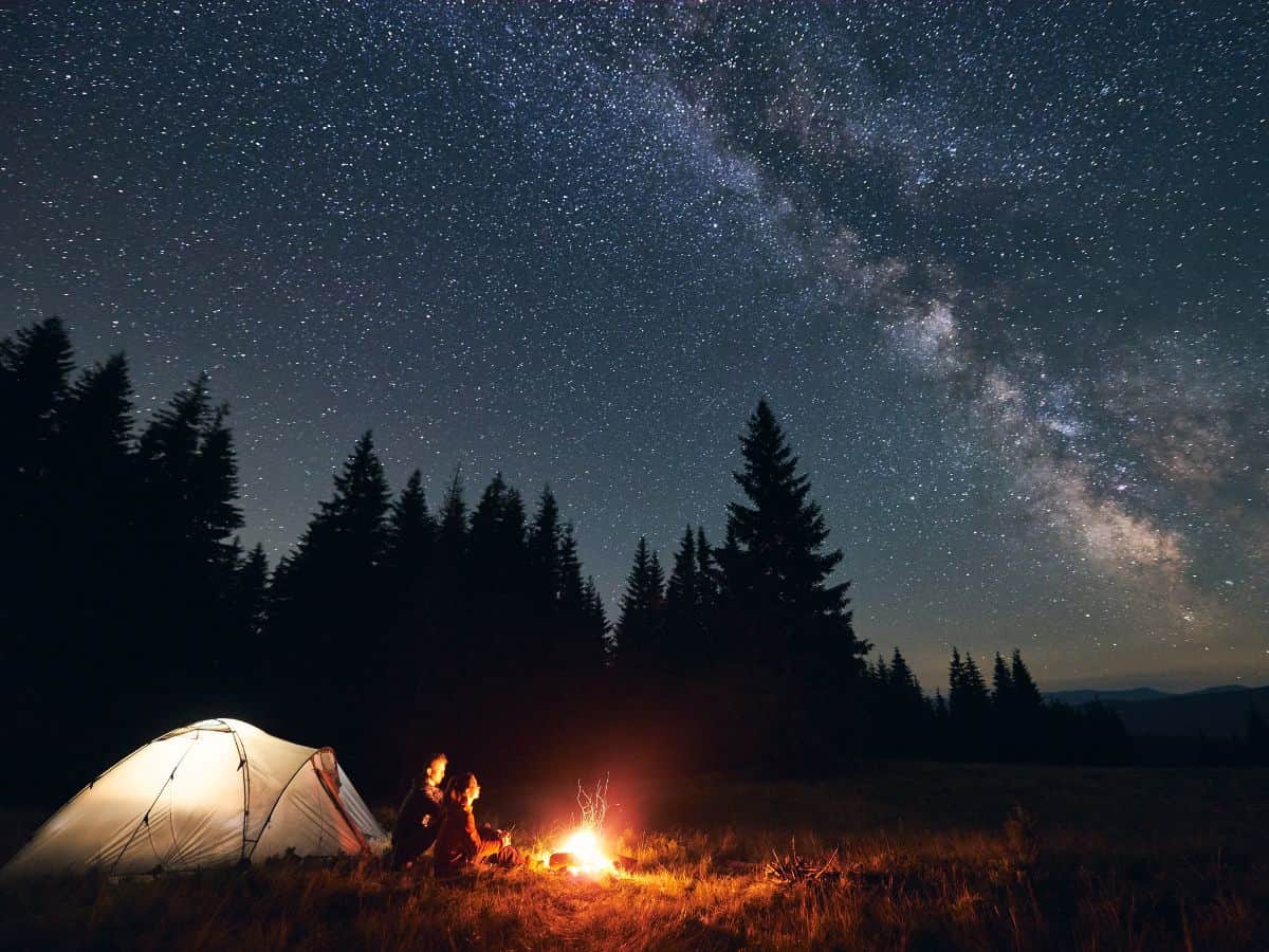 A person stargazes by a campfire under the milky way, contemplating their place in the universe.
