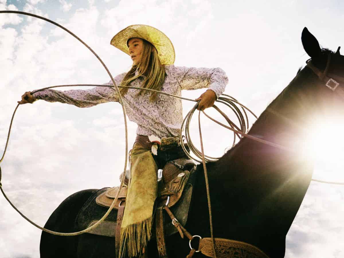 A cowgirl in a cowboy hat is lassoing a horse.