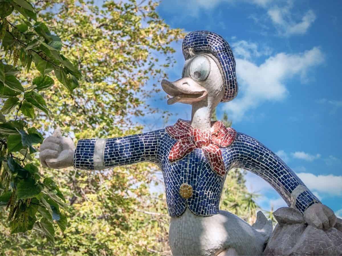 A statue of donald duck in front of a tree.