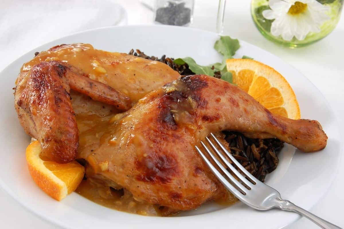 A white plate with chicken and oranges on it.