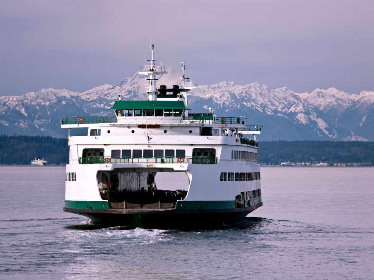 A ferry is traveling on the water with mountains in the background.