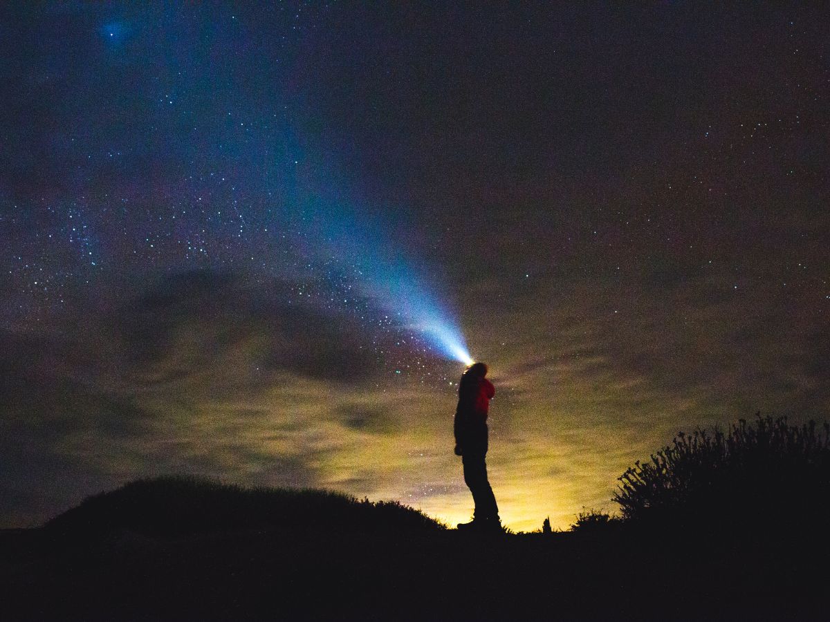 A person captivated by the night sky, stargazing with a flashlight.