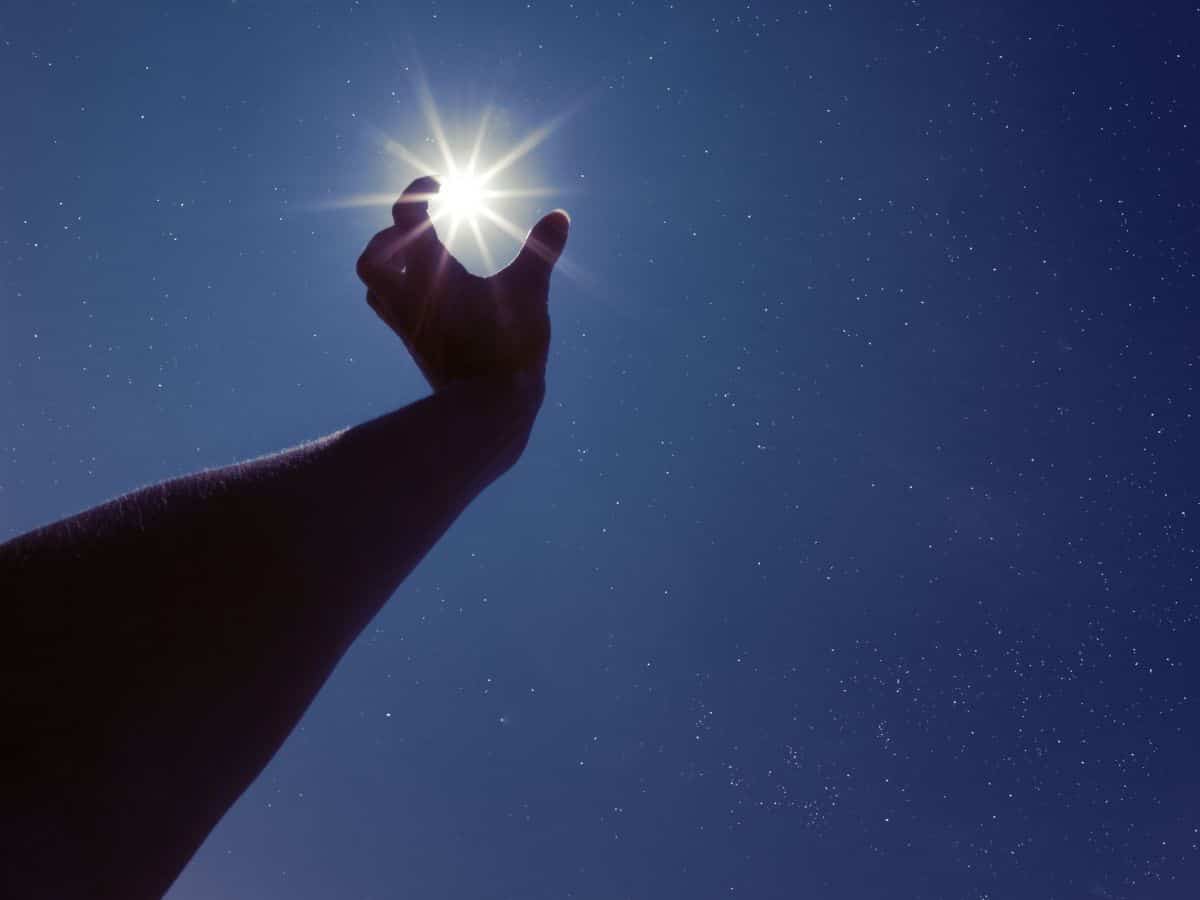 A person's hand reaching up to the sun in the night sky, contemplating stargazing.