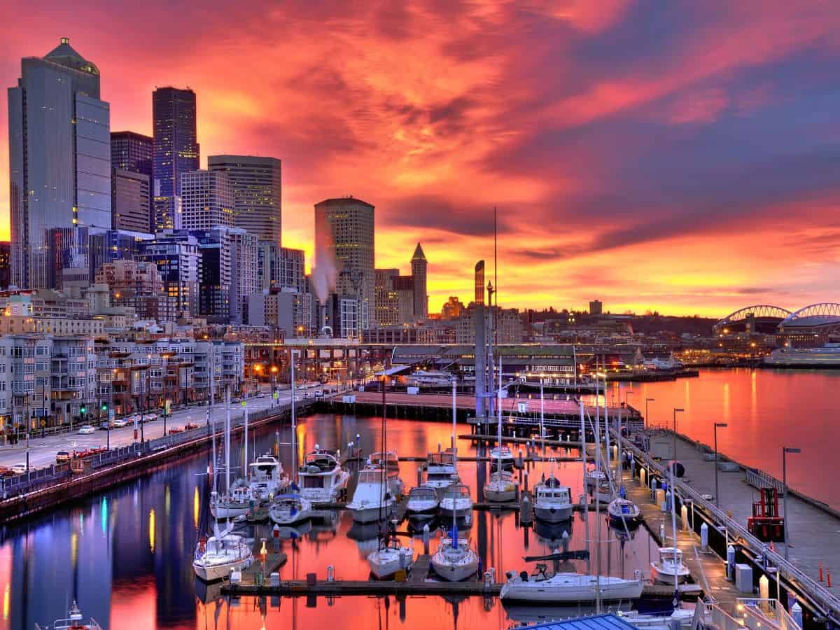 A colorful sunset over a harbor with boats and skyscrapers in Seattle.