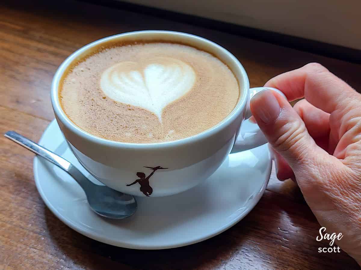 A hand holding a cup of coffee with a heart shaped latte art.