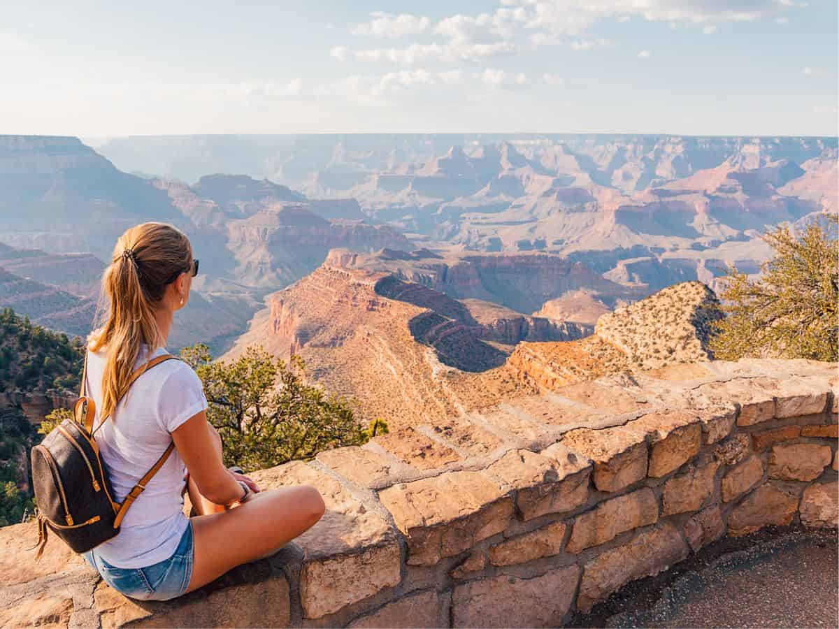 A woman is sitting on a ledge overlooking the grand canyon.