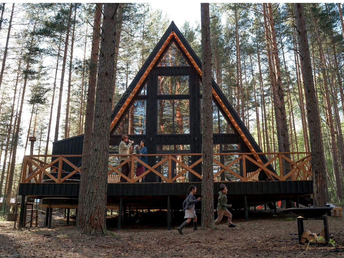 An a-frame cabin in the woods with a wooden deck.