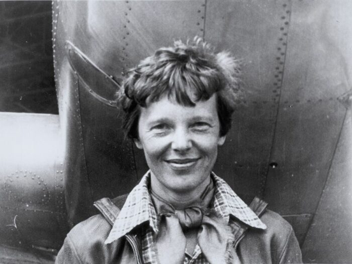 Amelia Earhart standing in front of an airplane with a smile.