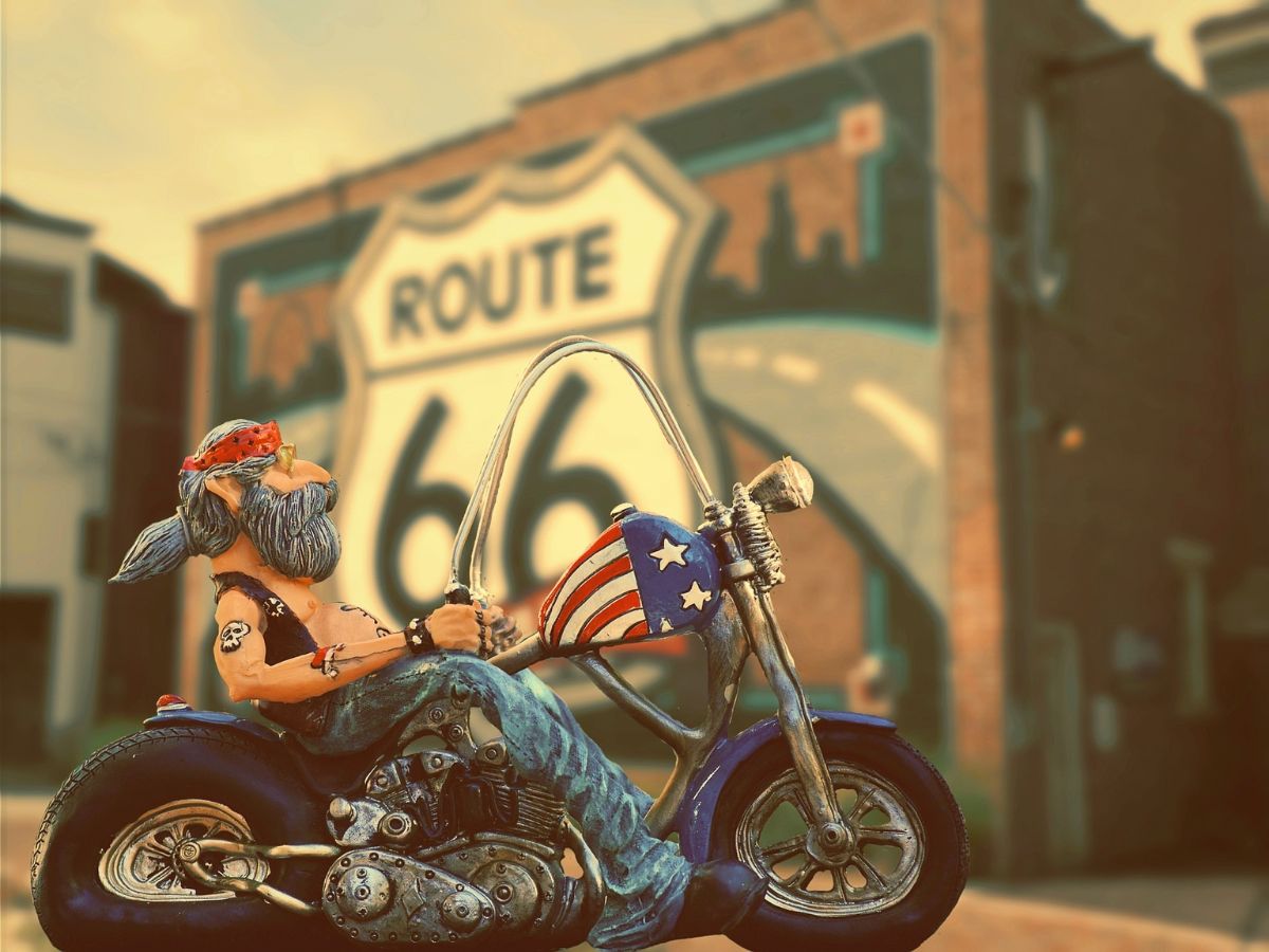 A statue of a biker sitting on a motorcycle by a Route 66 sign.