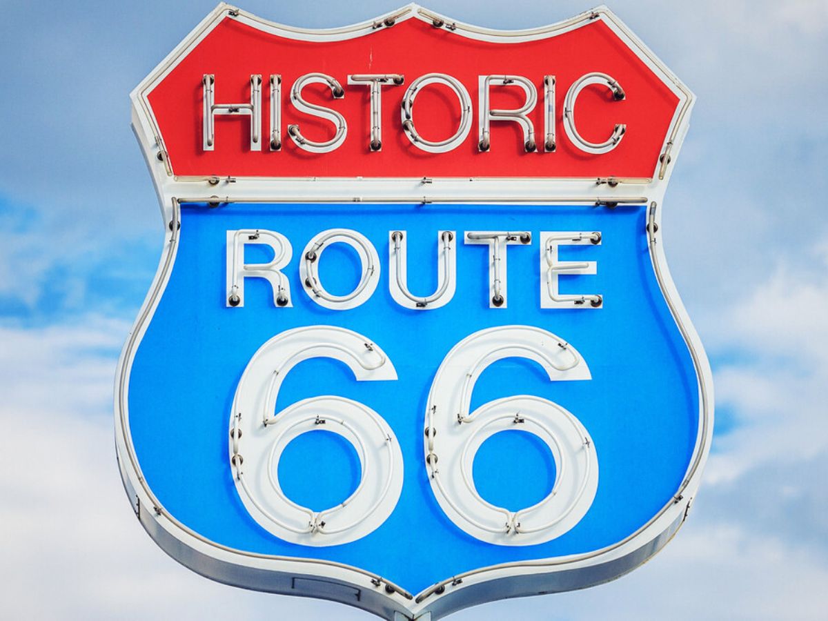 A neon sign for historic route 66 sign against a blue sky.
