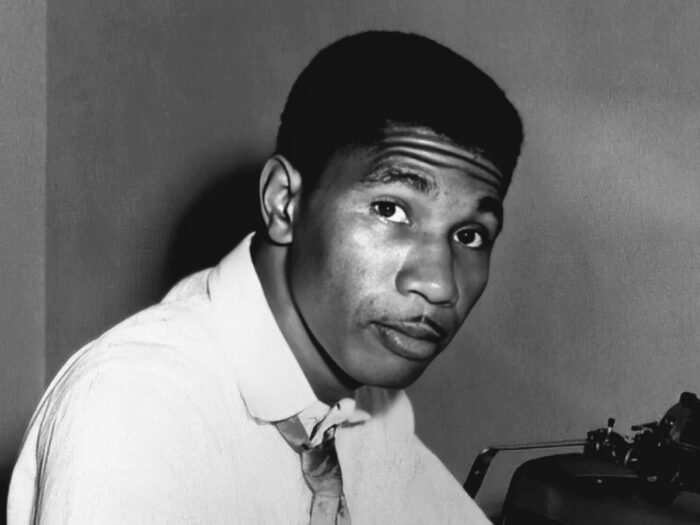A black and white photo of Medgar Evers sitting by a typewriter.