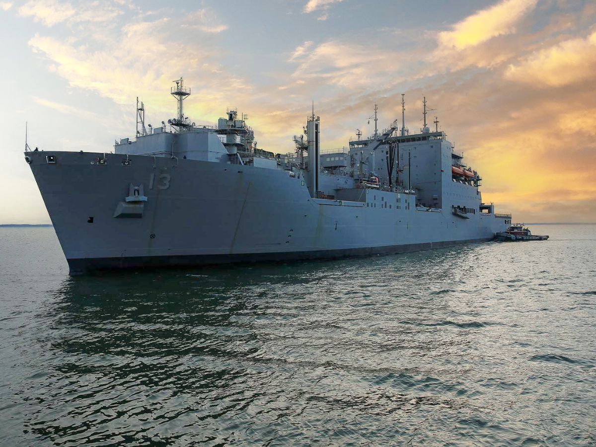 A large navy ship in the water at sunset.