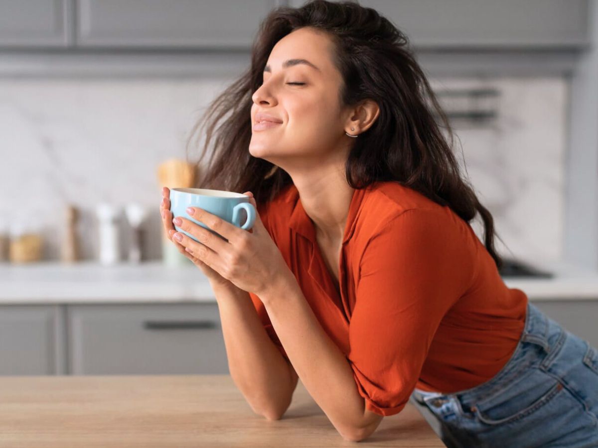 A woman leaning over a kitchen counter while holding a cup of coffee.