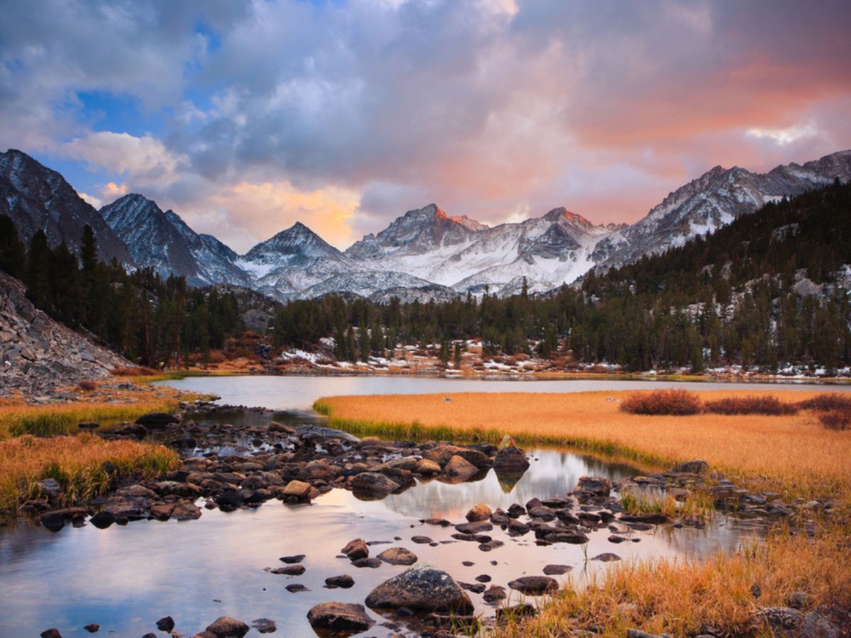 A serene mountain landscape at sunset with snow-capped peaks, a reflective river, and colorful skies.