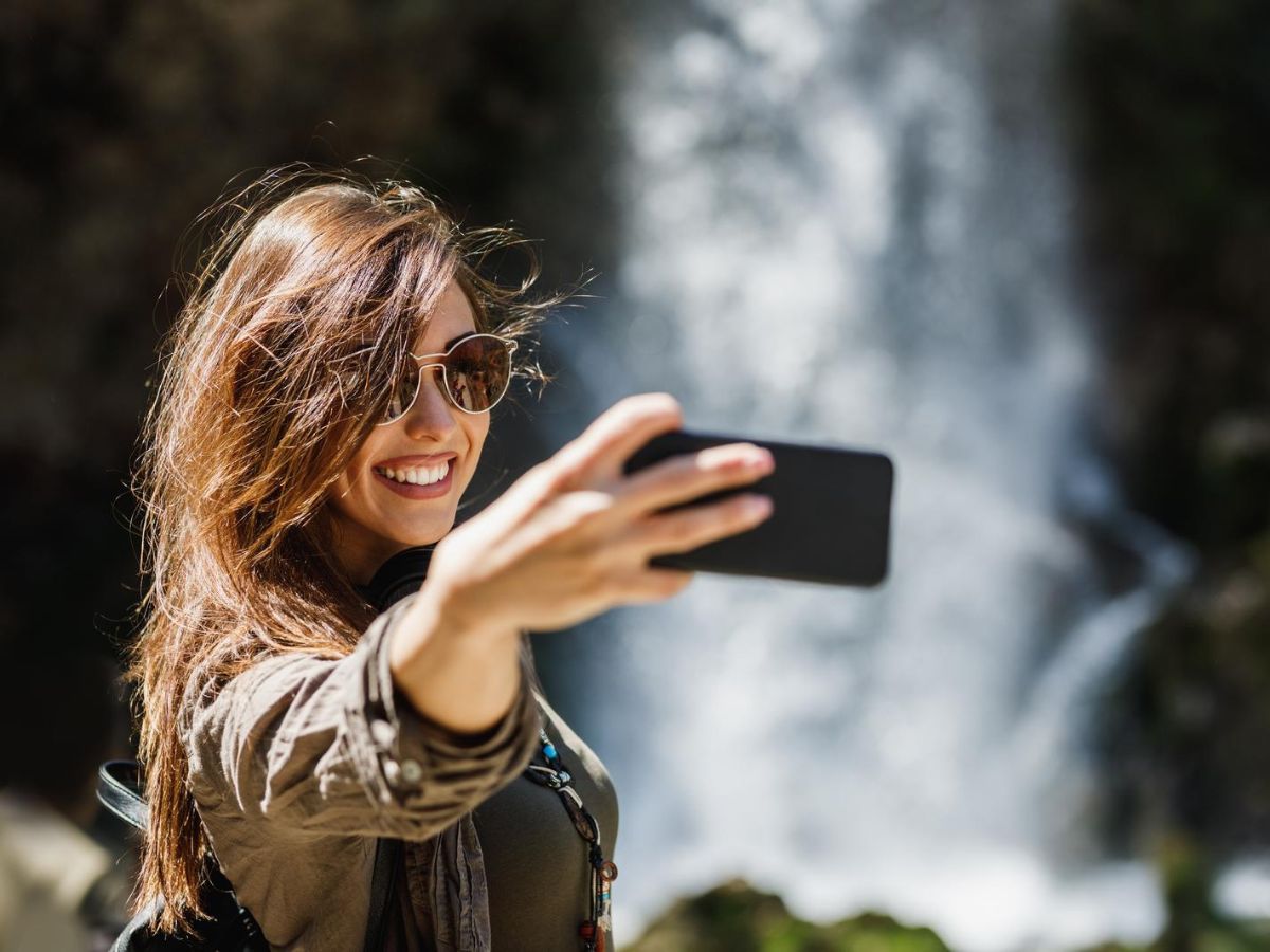 A woman taking a selfie in front of a waterfall.