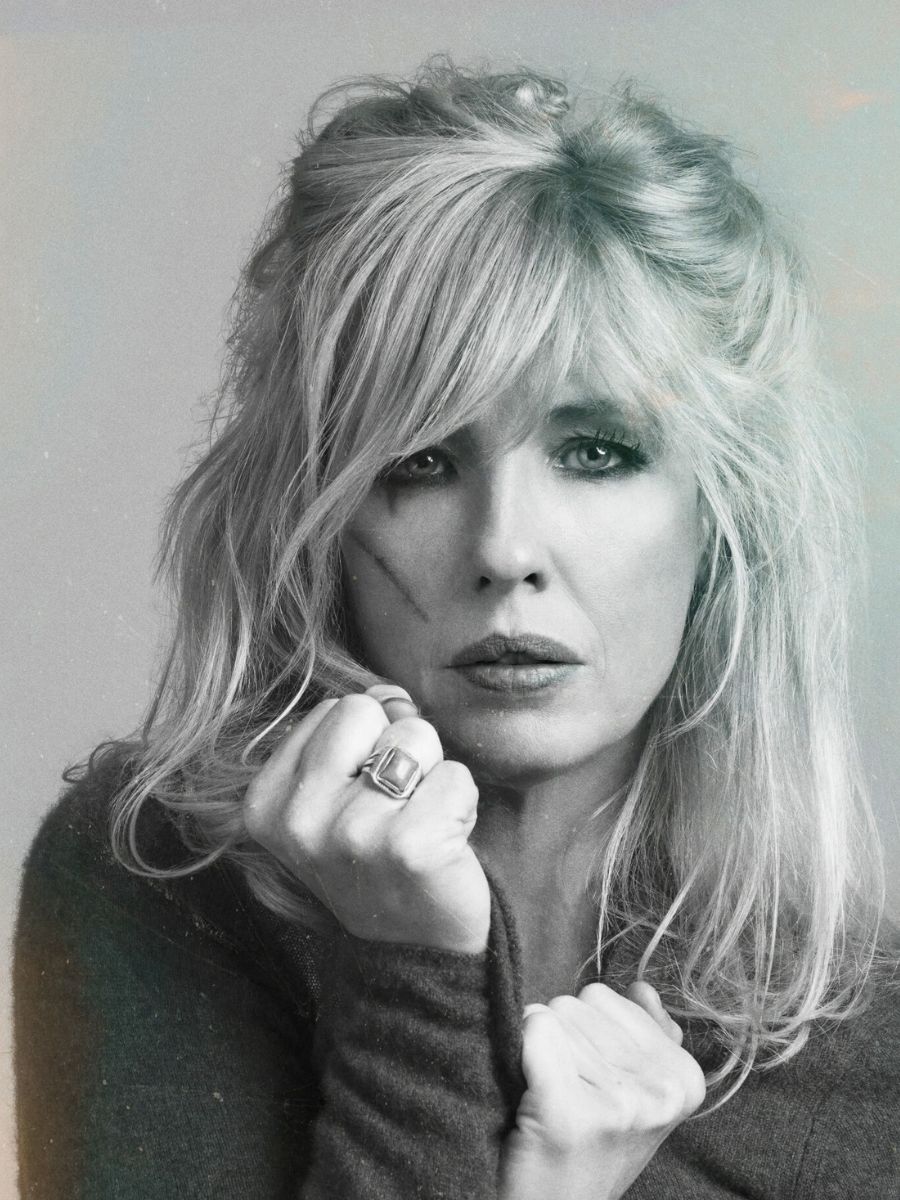 Black and white portrait of a pensive woman with blonde hair holding her chin, wearing a turtleneck and a ring.