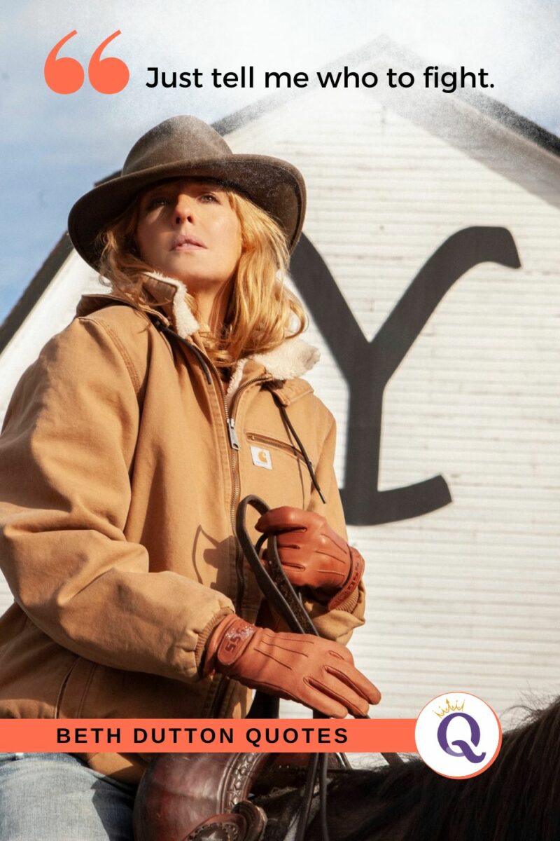 Beth Dutton in a wide-brimmed hat and tan jacket stands confidently in front of a white barn.
